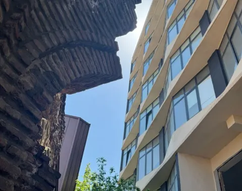 Historische Backsteinmauer im Kontrast zu einem modernen, wellenförmigen Glasgebäude bei Tageslicht.