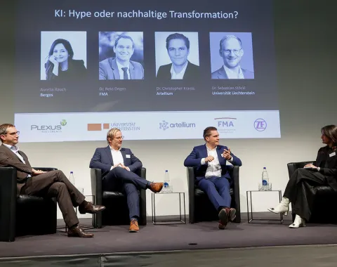 Eine Podiumsdiskussion an der Universität Liechtenstein über Künstliche Intelligenz mit vier Personen auf der Bühne. Im Hintergrund sind Porträts und Namen der Redner auf einer Leinwand zu sehen.