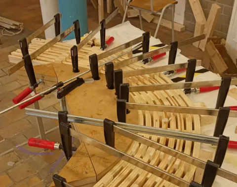 Ein Holzmodell eines Möbelstücks wird mit mehreren Schraubzwingen auf einem Tisch fixiert. Das Bild zeigt den handwerklichen Prozess der Studierenden während der «Maak Week» an der Universität Antwerpen.