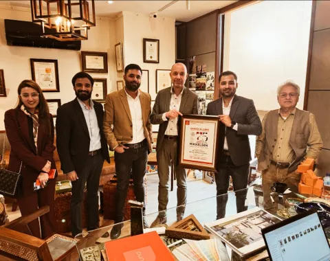 Eine Gruppe von sechs Personen steht in einem Büro, eine Person hält eine gerahmte Auszeichnung. Im Hintergrund sind Zertifikate und Auszeichnungen an der Wand zu sehen.