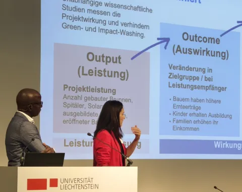 Zwei Personen präsentieren auf der Bühne des 16. Liechtensteinischen Stiftungsrechtstags 2024 im Auditorium der Universität Liechtenstein. Sie stehen vor einer Leinwand mit einer Präsentation über Chancen und Herausforderungen in der Sozial- und Wirtschaftswissenschaft. Ein Rednerpult mit dem Logo der Universität ist im Vordergrund sichtbar.