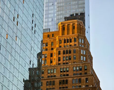 Moderne und historische Architektur in New York City, mit einem markanten Backsteingebäude im Vordergrund und gläsernen Hochhäusern im Hintergrund. Symbolisiert den Kontrast und die Vielfalt der Stadt.