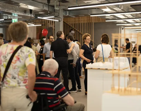 Besucherinnen und Besucher erkunden den neuen Standort der Universität Liechtenstein während des Tags der offenen Tür. Menschen stehen in einem modernen Innenraum, unterhalten sich und betrachten Ausstellungsstücke.