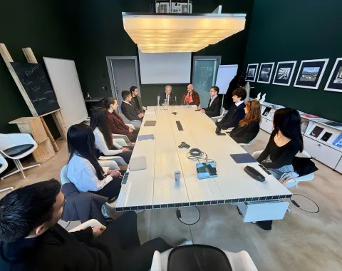 Besprechung in einem modernen Konferenzraum an der Universität Liechtenstein. Eine Gruppe von Personen sitzt um einen langen Tisch, darunter akademische Vertreter und Studierende. An den Wänden hängen Bilder, und im Raum steht eine Tafel.