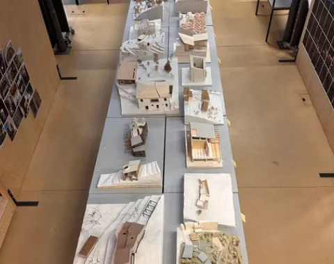 Eine Reihe von Architekturmodellen auf Tischen in einem Studio. Die Modelle zeigen verschiedene Gebäude und Landschaften, die im Rahmen eines Projekts des Advanced Studios Upcycling der Universität Liechtenstein erstellt wurden. Im Hintergrund sind Regale und weitere Arbeitsbereiche zu sehen.