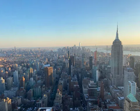 Luftaufnahme von New York City bei Sonnenuntergang, mit dem Empire State Building im Vordergrund und der Skyline im Hintergrund.