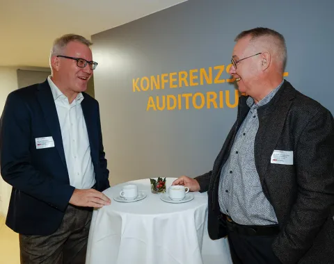 Zwei Männer im Gespräch bei einer Veranstaltung an der Universität Liechtenstein. Sie stehen an einem Stehtisch mit Kaffeetassen im Bereich "Konferenzzentrum Auditorium".