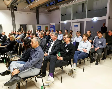 Eine Gruppe von Menschen sitzt in einem modernen Konferenzraum der Universität Liechtenstein. Sie hören aufmerksam einem Vortrag zu, der sich mit den Herausforderungen und Chancen der Nachhaltigkeitsregulierung für kleine und mittelständische Unternehmen befasst.