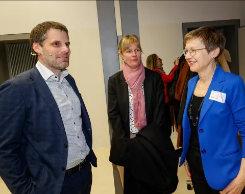 Drei Personen unterhalten sich bei einer Veranstaltung an der Universität Liechtenstein. Eine Frau trägt einen blauen Blazer, eine andere einen schwarzen Mantel mit rosa Schal, und der Mann trägt ein dunkelblaues Sakko.