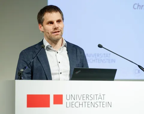 Der Rektor der Universität Liechtenstein Christian Frommelt steht an einem Redepult mit dem Logo der Universität aufgedruckt.