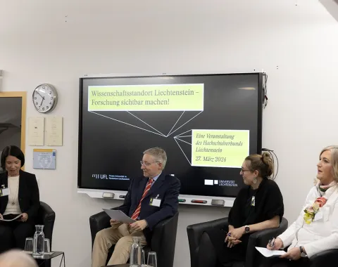 Podiumsdiskussion an der Universität Liechtenstein mit vier Personen, die auf Stühlen sitzen. Im Hintergrund ist ein Bildschirm mit der Aufschrift "Wissenschaftsstandort Liechtenstein – Forschung sichtbar machen" und dem Datum der Veranstaltung zu sehen.
