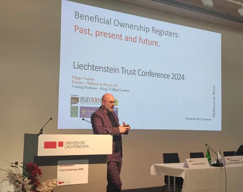 Ein Redner steht vor einem Podium mit dem Logo der Universität Liechtenstein und präsentiert bei der Liechtenstein Trust Conference 2024. Im Hintergrund ist eine Projektion mit dem Titel "Beneficial Ownership Registers: Past, present and future" zu sehen.