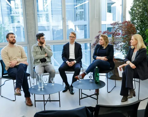 Podiumsdiskussion an der Universität Liechtenstein: Fünf Personen sitzen in einem modernen Raum mit großen Fenstern und Pflanzen, diskutieren über den Wohnungsmarkt. Vor ihnen stehen Tische mit Wassergläsern und einer Flasche.