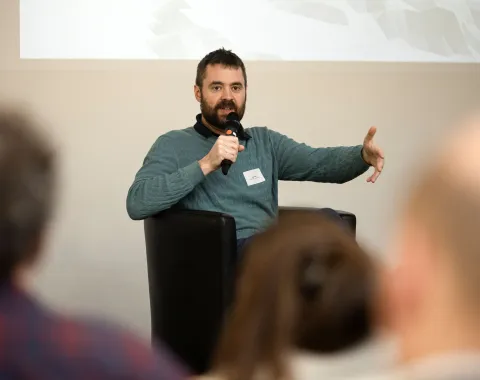 Mann mit blauem Pullover auf Podium mit Mikrofon