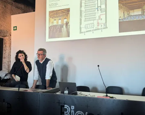 Zwei Personen tragen etwas vor mit einer Beamerprojektion im Hintergrund