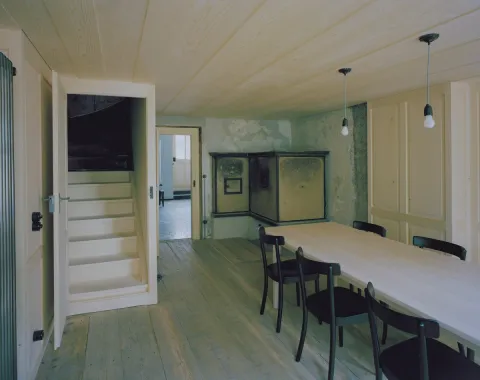 Minimalistischer Innenraum mit Holztisch und historischem Ofen in renoviertem Gebäude