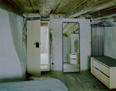 Rustikales Schlafzimmer mit Holzbalkendecke, Spiegel und schlichten Möbeln in renoviertem Altbau