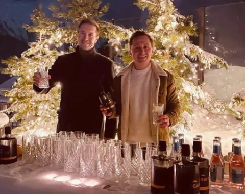 Winterliche Outdoor Bar mit Getränken und zwei Personen vor beleuchtetem Weihnachtsbaum bei Networking Event
