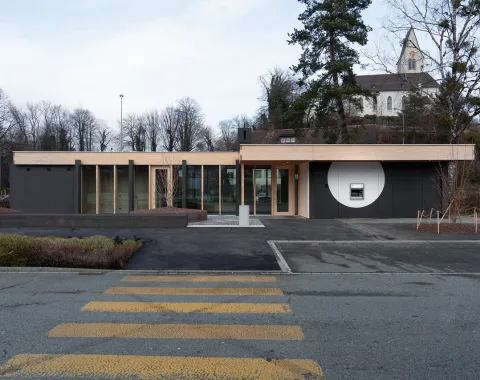 Zeitgenössisches Flachbau Gebäude mit klarer Linienführung vor Kirche und Strassenraum Architekturaufnahme