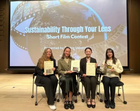Vier weibliche Personen sitzen auf einem Stuhl und halten ein Zertifikat in der Hand