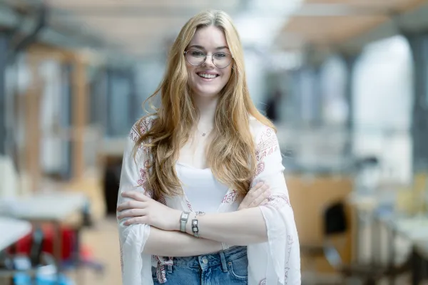 Studentin der Universität Liechtenstein mit weissem Pullover lächelt in die Kamera – Campusaufnahme in freundlicher Lernumgebung