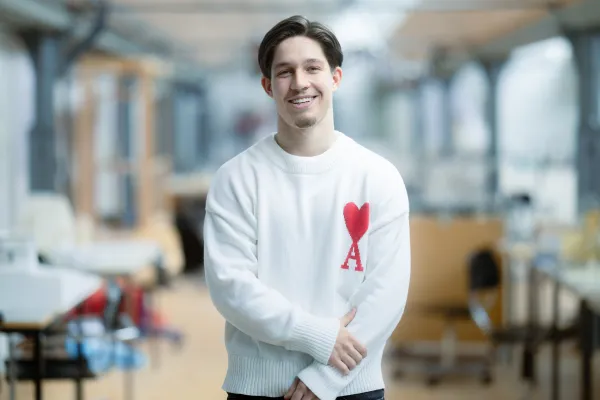 Student der Universität Liechtenstein mit weissem Pullover lächelt in die Kamera – Campusaufnahme in freundlicher Lernumgebung