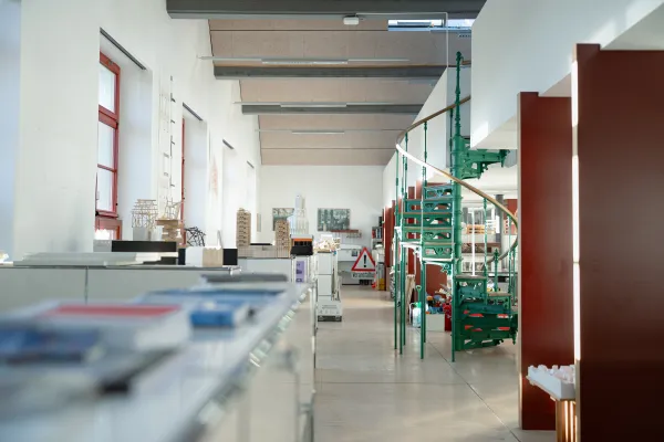 Innenaufnahme eines hellen Architekturstudios an der Universität Liechtenstein mit Modellen, Zeichnungen und einer grünen Wendeltreppe im Fokus.