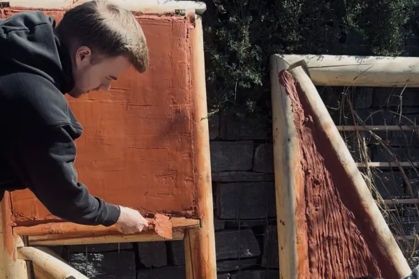 ZweiStudierende füllen einen Holzrahmen mit rot eingefärbtem Lehm