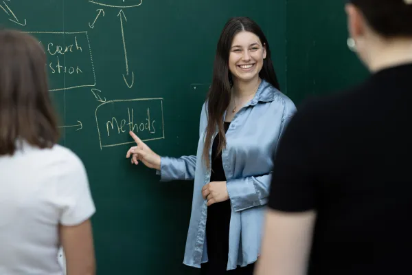 Studierende präsentieren ein Forschungskonzept an der Tafel und diskutieren Methoden an der Universität Liechtenstein.