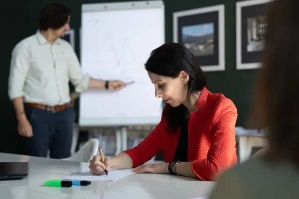 Dozent präsentiert mathematische Funktion an Flipchart, während eine Teilnehmerin aktiv mitschreibt.
