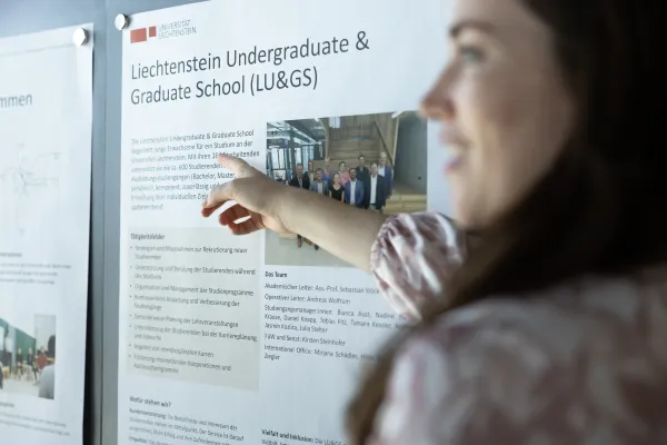 Studentin zeigt auf ein Poster der Liechtenstein Undergraduate & Graduate School an der Universität Liechtenstein.