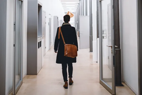 Studierende*r durchquert lichtdurchfluteten Hochschulflur der Universität Liechtenstein mit Dialektschrift an der Decke – modernes Campusambiente mit regionalem Bezug.