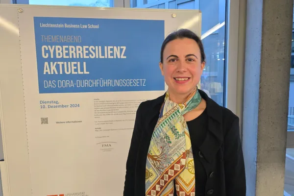 Frau steht lächelnd vor einem Plakat der Liechtenstein Business Law School. Das Plakat kündigt den Themenabend „Cyberresilienz aktuell: Das DORA-Durchführungsgesetz“ an, der am 10. Dezember 2024 stattfindet.