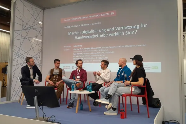 Podiumsdiskussion auf der Messe «Holz Handwerk 2024» in Nürnberg. Fünf Personen sitzen auf einer Bühne vor einer Leinwand mit dem Titel "Machen Digitalisierung und Vernetzung für Handwerksbetriebe wirklich Sinn?". Die Diskussion thematisiert die Rolle der Digitalisierung im Handwerk.