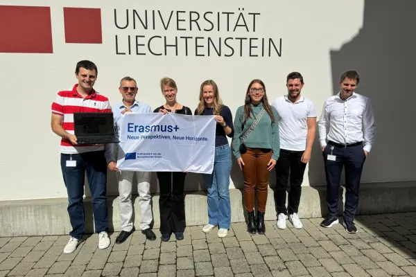 Eine Gruppe von sieben Personen steht vor einem Gebäude mit dem Schriftzug "Universität Liechtenstein". Sie halten ein Banner mit der Aufschrift "Erasmus+ Neue Perspektiven, Neue Horizonte".
