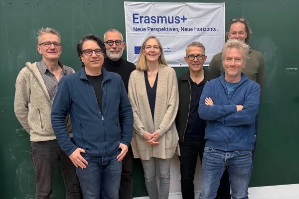 Eine Gruppe von acht Personen steht vor einem grünen Hintergrund. Sie lächeln in die Kamera. Im Hintergrund hängt ein Banner mit der Aufschrift "Erasmus+ Neue Perspektiven, Neue Horizonte".