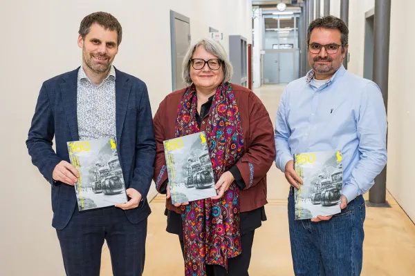 Drei Personen stehen in einem Flur und halten das Forschungsmagazin "160²" in den Händen. Das Magazin behandelt das Thema Künstliche Intelligenz.