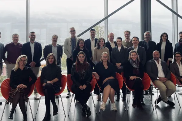 Gruppenfoto von Teilnehmenden der MiCAR Expert Roundtable Series an der Universität Liechtenstein. Die Personen stehen und sitzen in zwei Reihen vor einer großen Fensterfront mit Blick auf eine bergige Landschaft.