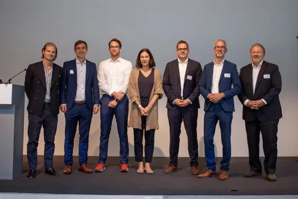 Eine Gruppe von sieben Personen steht auf einer Bühne beim 8. Liechtenstein Workshop of Sustainable Finance an der Universität Liechtenstein. Sie tragen formelle Kleidung und lächeln in die Kamera.