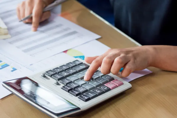 Person sitzt am Tisch mit Taschenrechner und Papier und rechnet