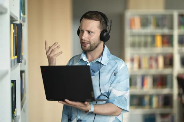 Student mit Laptop und Headset im Bibliotheksbereich der Universität Liechtenstein während eines Online-Meetings.