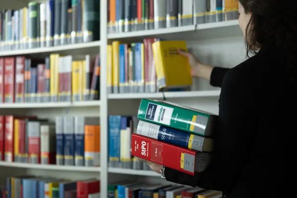 Frau stellt gelbes Fachbuch ins Regal und hält weitere juristische Bücher in der Bibliothek der Universität Liechtenstein.