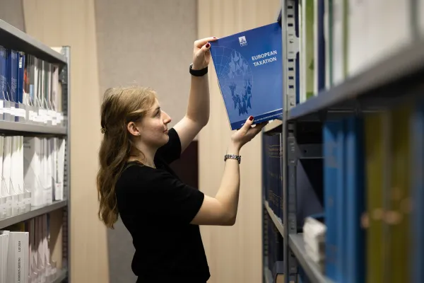 Frau holt Zeitschrift European Taxation aus Regal in der Bibliothek der Universität Liechtenstein.