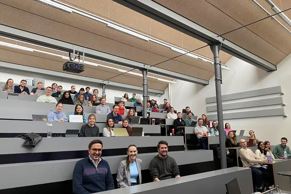 Eine Gruppe von Studierenden sitzt in einem modernen Hörsaal der Universität Liechtenstein. Sie nehmen an der Accenture Campus Innovation Challenge teil, einem Wettbewerb zur Entwicklung innovativer KI-Anwendungen. Die Studierenden lächeln und arbeiten an Laptops.