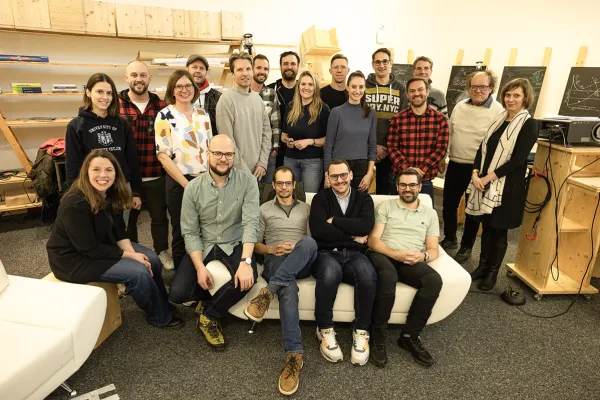 Gruppenfoto von Absolventen des Masterprogramms in Entrepreneurship der Universität Liechtenstein, die sich in einem Raum mit Regalen und Tafeln versammelt haben. Die Personen lächeln und stehen oder sitzen in zwei Reihen.