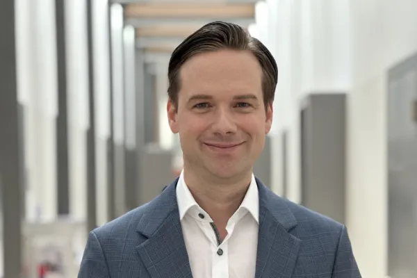 Ein Mann in einem blauen Anzug hält das Buch „Self-Leadership und Führung“ in einem modernen, hellen Flur.