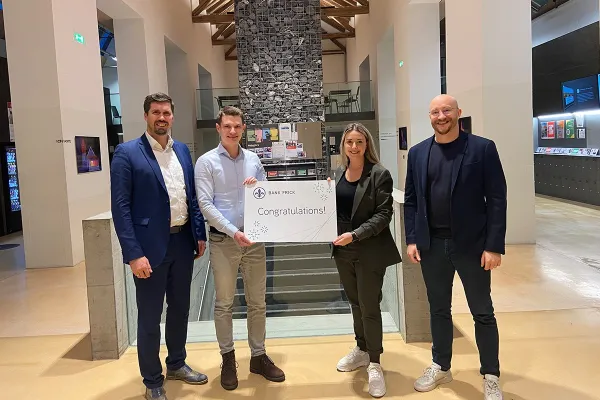 Vier Personen stehen in einem modernen Gebäude und halten ein Schild mit der Aufschrift "Congratulations!" von Bank Frick. Sie feiern die Vergabe eines Stipendiums für den Zertifikatsstudiengang Blockchain und FinTech an der Universität Liechtenstein.