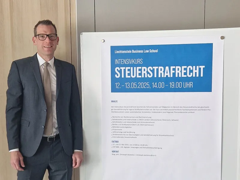 Ein Mann in Anzug steht neben einem Plakat, das den Intensivkurs „Steuerstrafrecht“ der Universität Liechtenstein ankündigt. Das Plakat enthält Informationen zu Datum, Uhrzeit und Inhalten des Kurses.